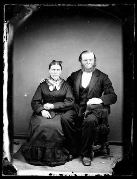 Full-length portrait of a bearded man and a woman sitting.