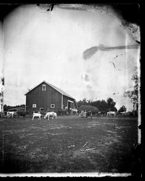 Family and animals, including horses and cattle with some apparent shorthorn markings, near the barn. Behind the group of two women and four children is a man standing on top of a horse-drawn wagon piled high with hay. On the left at the corner of the barn is a man on a horse-drawn mower, and a man on a horse-drawn dumprake.