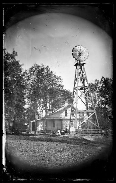 Family and baby carriage next to wooden tower windmill with house behind them. A.L. Dahl, landscape photographer, wagon, left.