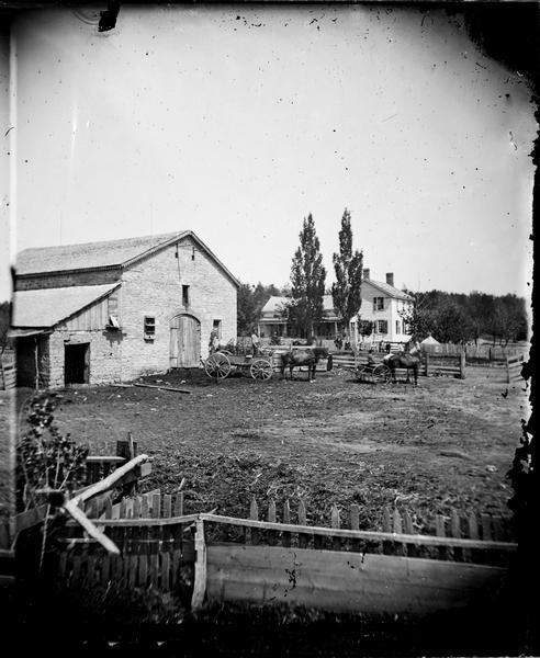 Stone barn with scalloped edging with people in wagons and house in background, picket fencing; in sec. 26, SE1/4. Biography in Biographical Review of Dane County, 1893, indicated Mr. Veerhusen was born in Hanover, Germany; identified from a stereograph at the Stoughton Historical Society; see also 1873 Plat of Dane County.