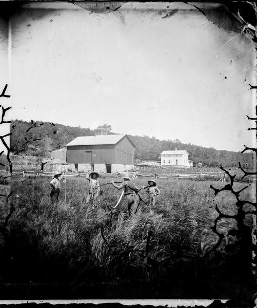 Three men and a boy in wheat field with scythes and a split-rail fence.  Barn with stone foundation and cupola and frame house in background; additional straw-topped structures.