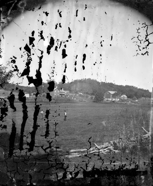 A field is in the foreground and further back is a log building, barn and house with people in the front yard.  Mr. Harold Haroldsen Stugaard died in 1875 and his wife, Berit Syverud, continued to farm the property located sec. 21 SE1/4, on Town Hall Road south of Offendahl Road. In 1903 this was the Martin Bang farm, in 1918 the house was moved from its foundation, in 1945 it was owned by John G. Bigler, in 1980 it was owned by Gary Lutz and in 1980 the house was demolished.