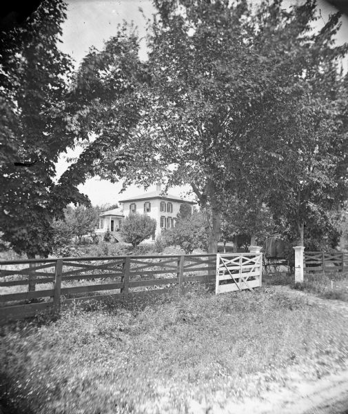 Brick house with well-landscaped property and unusual board fence. A.L. Dahl's photographic wagon is in the right foreground.