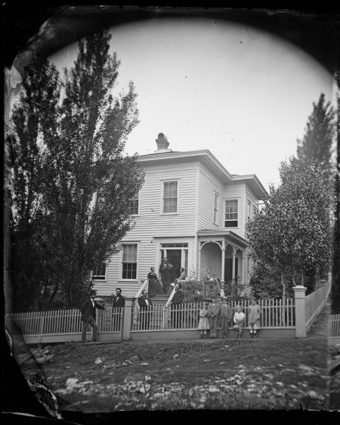 Six children and eight adults stand in front of the G. Klove house, with  a picket fence and small front porch.
