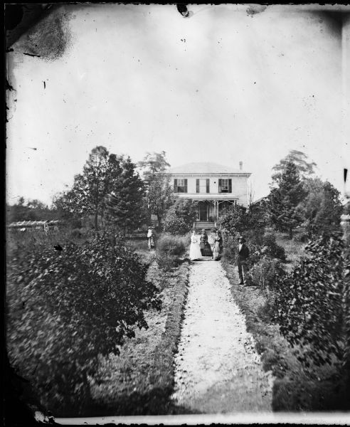 A view up a garden path leads past family members to a bracket-style frame house with outbuildings.