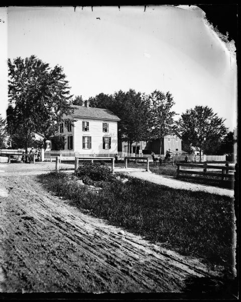 A dirt road leads to Dr. Blake's (probably Samuel M.) frame house in Lodi or Prairie du Sac. A family is under a tree near a wooden fence. On the right is a man in a pony cart.