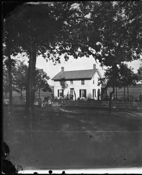 View of the superintendent's residence at the Wisconsin State Fish Hatchery (aka Nevin Fish Hatchery, 3911 Fish Hatchery Rd.), a frame house on a stone foundation in front. The house has two chimneys, one at each end, glass trim above front door and a porch in back covered with vines.