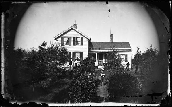 Boy on garden path holding bunny rabbit with family in front of frame house with shuttered windows and latticework trim above porch.