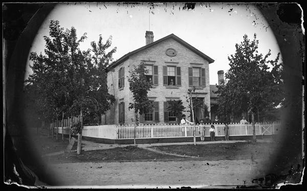John Theodore Parman and his wife Louise stand second and third from the left behind their home's fence. Their daughters can be seen in the windows and their sons in front of the fence. The names of these others in the photograph may well be, Albertine Seward (age 67) and Mathilda (age 37), with the children Rudolph (age 6), Herman, (age 4) and Mathilda, (age 2). Parman, a wheelwright, was the father-in-law of Emil Frautschi of Madison, Wisconsin.
