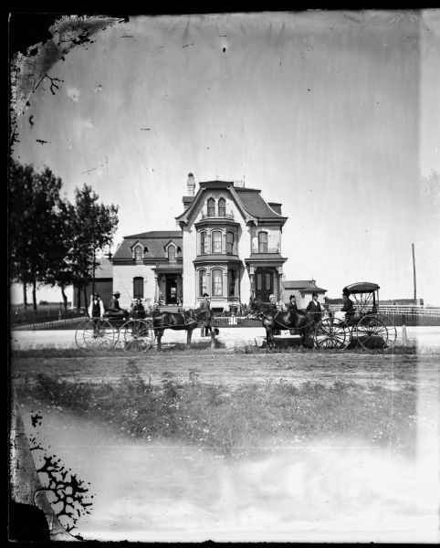 Group of people in front of iron fence with wagon and carriage; large brick mansardic house in background has large bay window on upper and lower stories, double front doors and iron fence trim on roof and porch roof. House was built for M.K. Dahl. The current owner (1975) Mr. James C. Laird owns the original plans for the house which is located at 314 Beaver Dam Street.