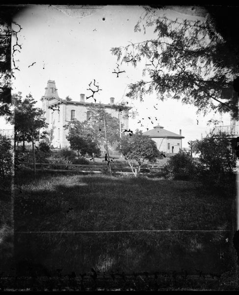 In the distance, women stand in front of the Norwegian Lutheran Seminary. On the right is an octagonal outbuilding, possibly a carriage house. The seminary was located next to Monona Academy on Madison's east side.