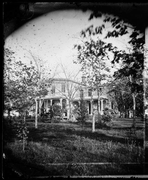 Family in yard with carriage with large stone house behind that has shutters closed. The house was built in 1845. Harmon J. Hill was the first supervisor of the Town of Madison. His property was later to become part of the University Hill Farms acreage.
