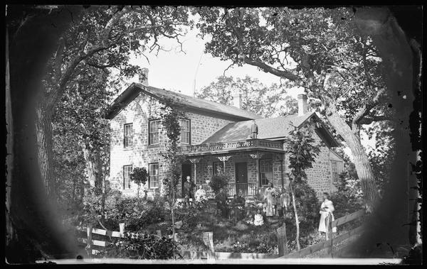 The William Bullock family is posed before a stone upright and wing house with carpenter's lace brackets and trim on its porch.