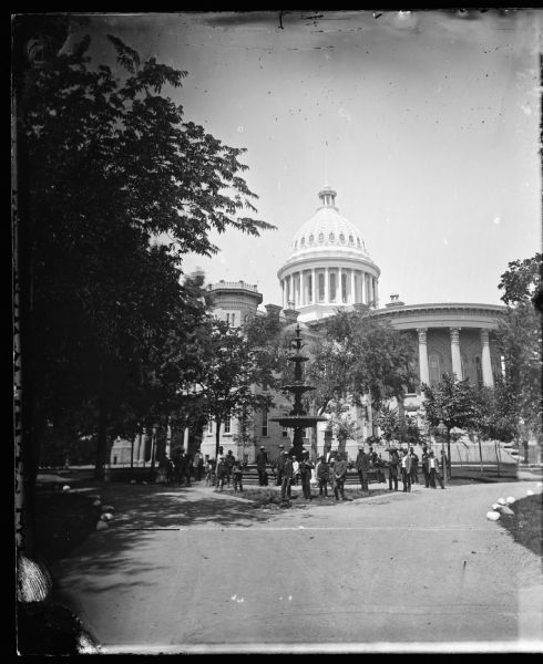 Group in front of the Centennial Fountain on Capitol Square. View of the capitol from Monona Avenue. The fountain is a replica of the Centennial Fountain erected in Philadelphia and was built in 1876.