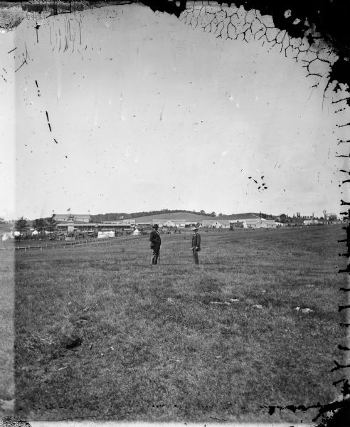 View looking west across the area once occupied by Camp Randall during the Civil War and towards the Breese Stevens farm property.  The Madison Centennial Fairgrounds buildings can be seen behind the two men in the middle distance.