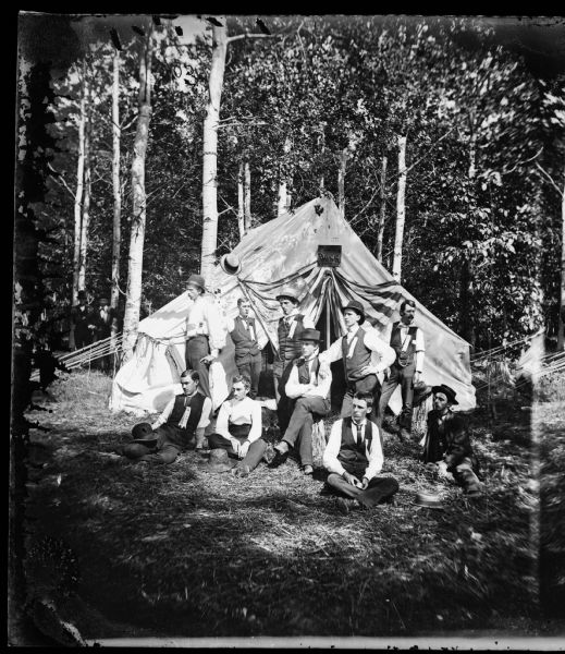 Group of men outside tent with "The Boss" sign above door and labels on some of the fellows' shirts saying, "CTC," an abbreviation for the Chicago Traveling Club. This is identified as trip #8 to Twin Lakes, Kenosha County, Wisconsin.