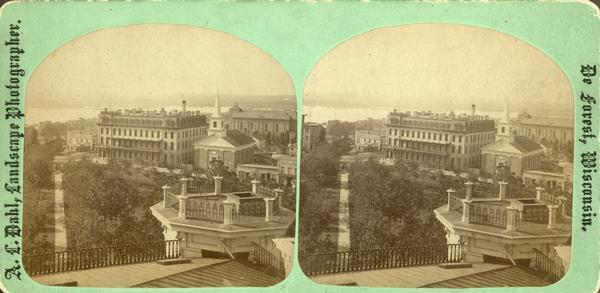 View of the Capitol Square from the roof of the Wisconsin State Capitol, looking south. The view includes the Park Hotel, The Baptist Church and St. Raphael's Catholic Church, on West Main Street with the steeple still under construction. A sign for "Cheap Dry Goods" can be seen in the left image. From the series, "The Beauties of Madison and Surroundings."