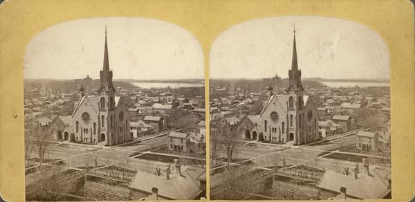 Elevated view towards the northwest across West Washington Avenue of the Congregationalist Church. Main Hall (now Bascom Hall) of the University of Wisconsin-Madison can be seen just left of center in the background, along with Lake Mendota on the right.