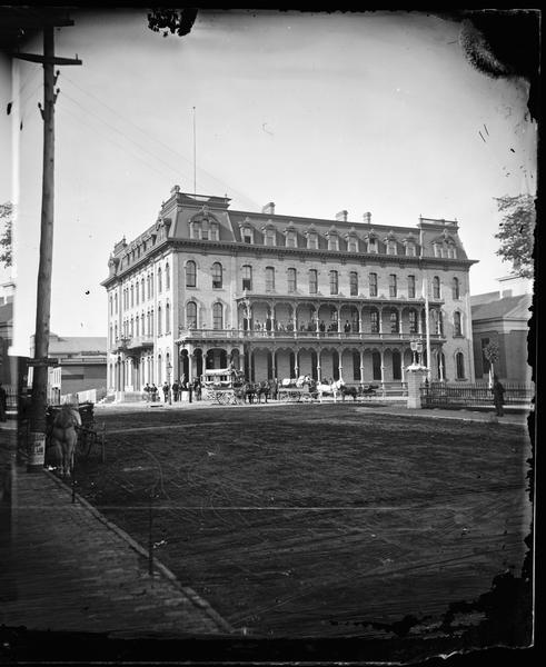 Park Hotel on the corner of Main and Carroll Streets. The Park Hotel wagon and baggage wagon are in front of the hotel. People are in front of the building and on the second floor balcony.