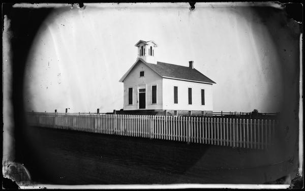 View of the Albion Prairie Methodist Episcopal Church, dedicated in 1868.  The church has a bell tower, a stone foundation, wide steps and a picket fence running in front.