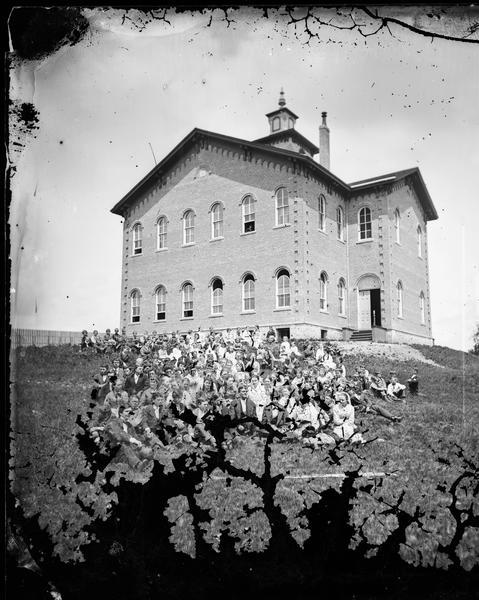 Lodi School was a three-story brick Romanesque building with a small cupola, built in 1868. It burned on March 28, 1878. It was rebuilt by December 1878, but burned again in 1886. A large crowd of boys and girls are seated on the ground, the older students in the front and younger in the rear.