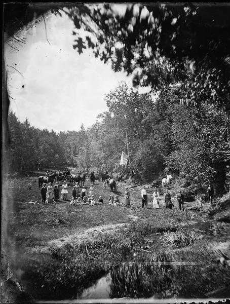 Group on picnic in field with carriages and flag.  Photograph for "G. Gunhus."