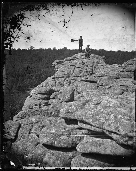 Two men on a rock formation in the Baraboo Bluffs. One man is holding out a hat.