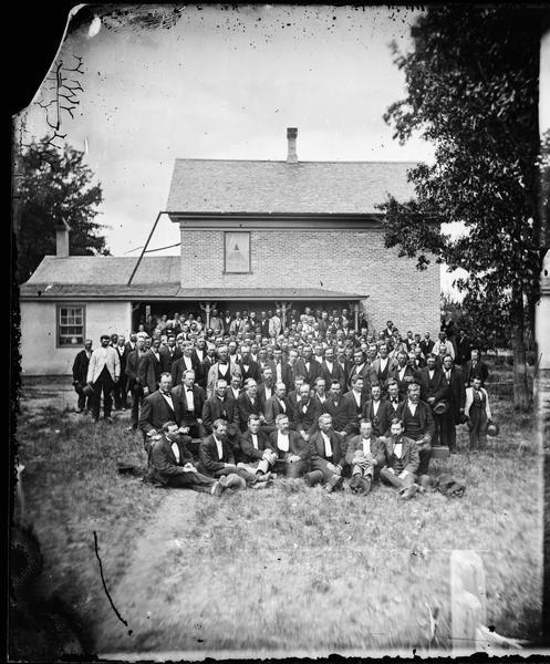 Group portrait of delegated to the Eastern District Norwegian Synod meeting held at Immanuel Norwegian Evangelical Lutheran Church, photographed in front of the church parsonage. Pastor Even Johnson Homme is in the second row, far left.