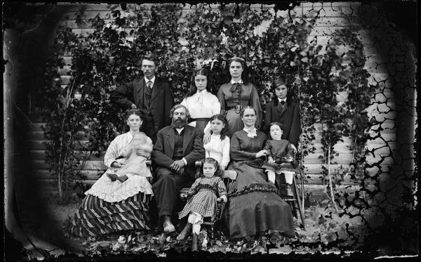 Group portrait of the William Bullock family, a group of eleven adults and children in front of an ivy covered wall.