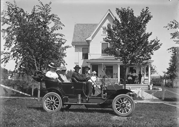 Home of Tina Dahl Bertrand. Lewis Dahl at the wheel of an automobile. Walter and mother second and third from right in back seat. Bertrands on porch.