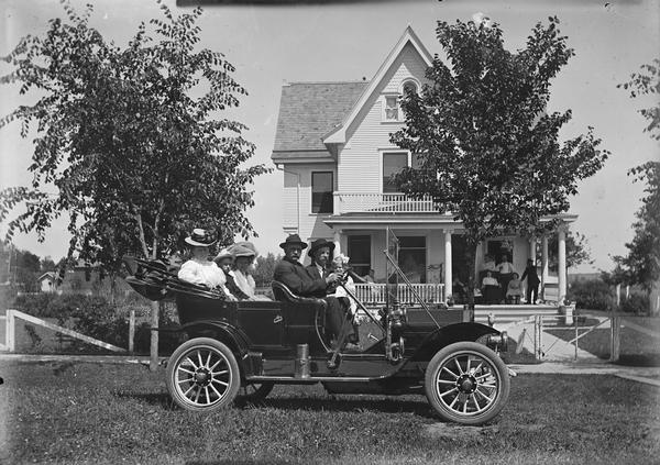 Lewis Dahl at the wheel of an automobile. Walter and mother second and third from right in back seat. This is the home of Tina Dahl Bertrand. Bertrands on porch.