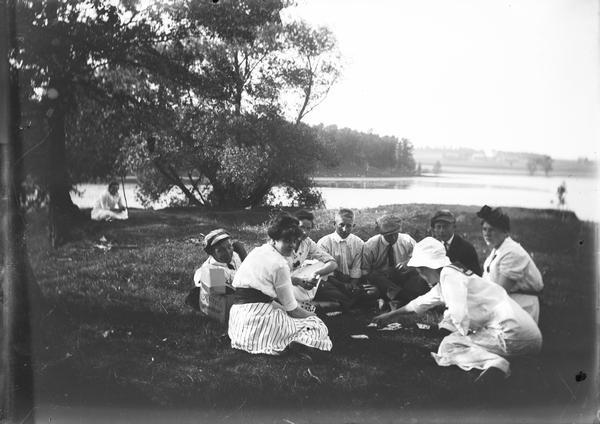 Outdoor seated group near lake shore playing cards at Walter Dahl's class reunion.