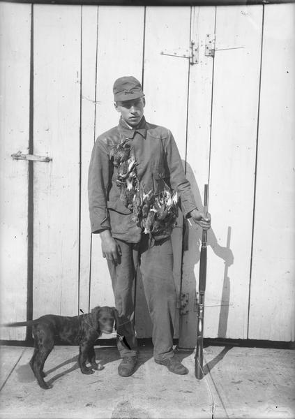 Walter Dahl with game birds strung around his neck. He is holding a rifle, and a young dog stands next to him.