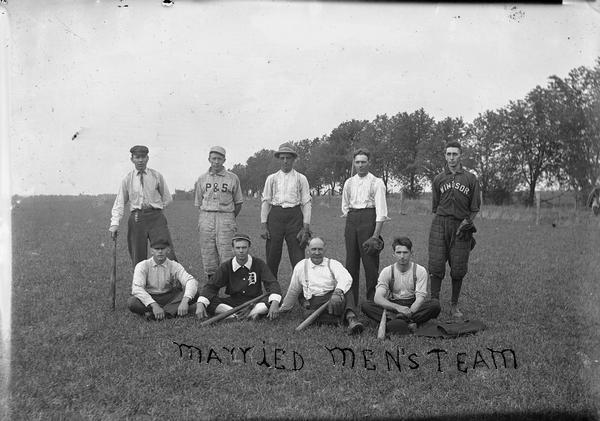 Outdoor group portrait of the Married men's baseball team. Nine men are posing, and one man on the far right has a Windsor insignia on his jacket.