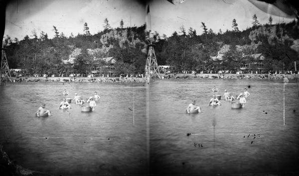 Swimming in the lake with the Cliff House in background. Cliff House was a resort hotel built shortly after 1872, when Devil's Lake was reached by rail. Boys are in barrels in the lake in foreground.