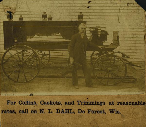 Photograph of N.L. Dahl in front of a horse-drawn hearse. Photograph is mounted on an advertising card reading: "For Coffins, Caskets, and Trimmings at reasonable rates, call on N.L. DAHL, De Forest, Wis." (aka DeForest.)