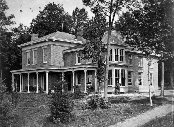 The Halle Steensland home, an impressive two-story brick house in Maple Bluff, with five family members posed along the front porches. It is possible this photograph was taken in connection with the completion of the house's new right wing. The house and farm was purchased by Senator Robert M. La Follette, Sr., and it is more commonly known today in association with the La Follette name.