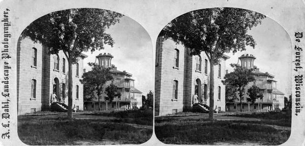 In the foreground stands the Monona Academy and in the background the Norwegian Lutheran Seminary, housed in the octagonal former Soldiers' and Orphans' home on Madison's east side. This view is mentioned in Dahl's 1877 "Catalogue of Stereoscopic Views" as "The whole place in one view."