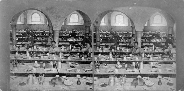 Women kitchen staff posed by tables set for a meal at Luther College. "View of the Dining Hall" as identified in Dahl's 1877 "Catalogue of Stereoscopic Views."
