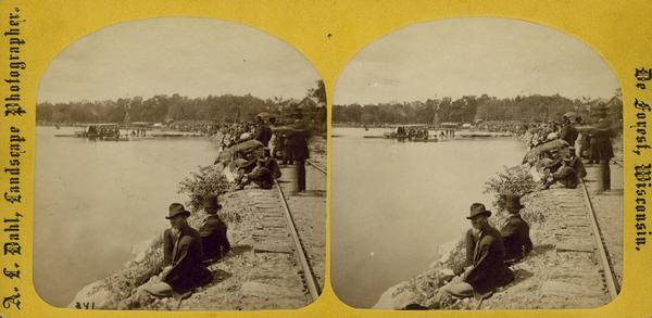 "The Grand Regatta, at Devil's Lake, June 21st & 22nd, 1877." Spectators sit on the railroad bed at Devil's Lake.