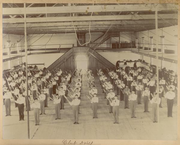 Male students performing a club drill inside the gymnasium at the Indian Industrial School.