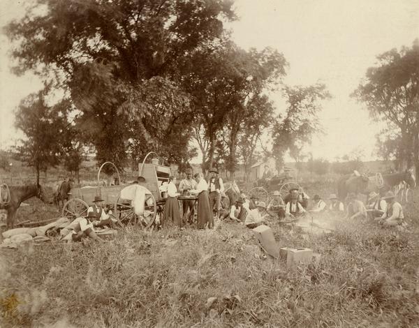 A chuck wagon and supper at a cowboy roundup.  A group of men sit around a fire.