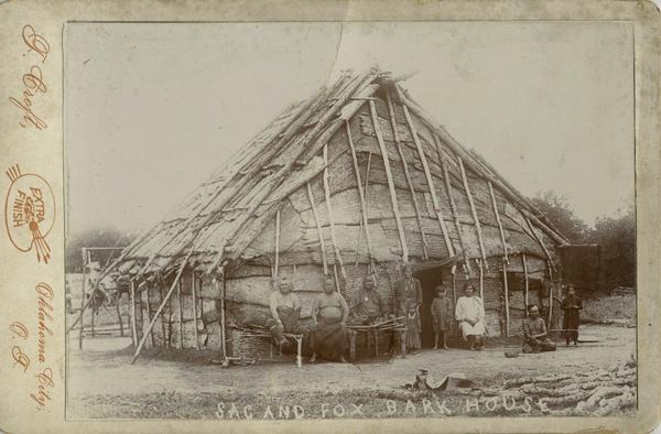 Members of the Mesquaki nation are posed outside of a Sac and Fox bark house.