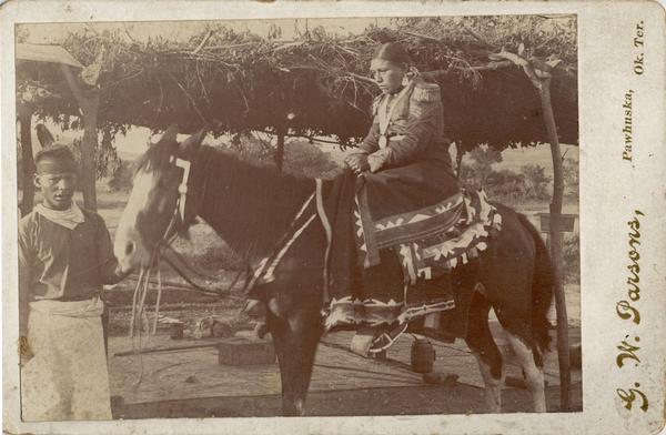 An Osage woman prepares to be married to the corn.  A man leads her horse.