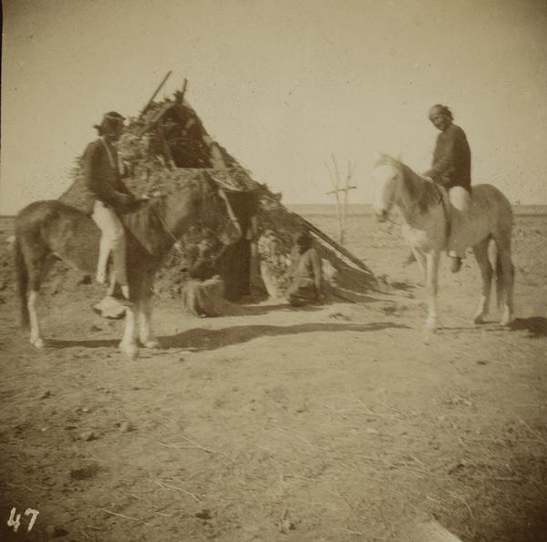 A Navajo Indian winter residence. Two men on horses gather outside.