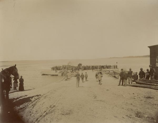 People on a boat dock watch a boat landing as part of the Ojibwa-Pillager Battle at Sugar Point on Bear Island.