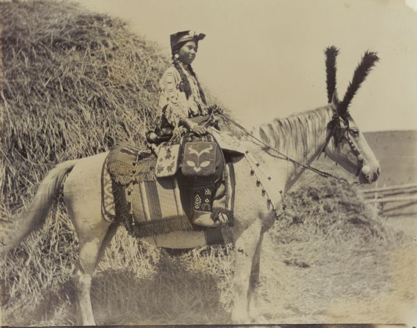 An Indian woman in full dress is on horseback at the Warm Springs Agency in Oregon.