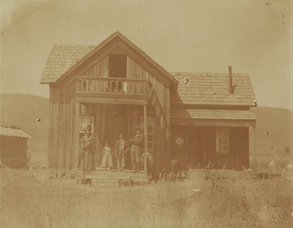 An Indian family in front of a wooden housing structure at the Warm Springs agency in Oregon.