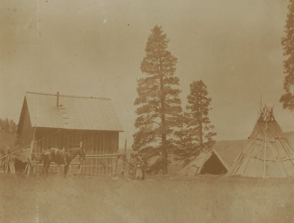 An Indian family with a wooden structure and a teepee at the Warm Springs Agency in Oregon.