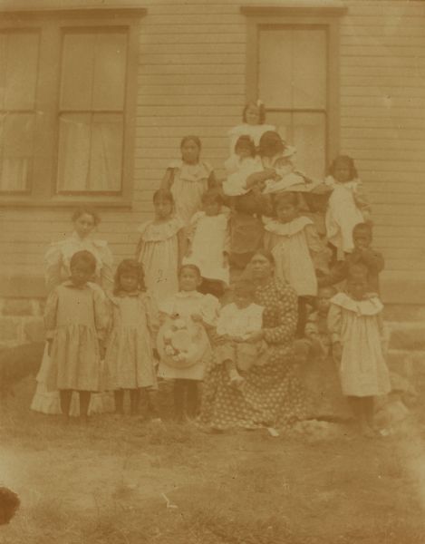 Mrs. Briggs, the matron, and Mrs. Pit, her assistant, gather with young girls in front of the dormitory at the Warm Springs Agency in Oregon.